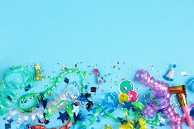 Colorful serpentine streamers, confetti and party horn on light blue background, flat lay. Space for text