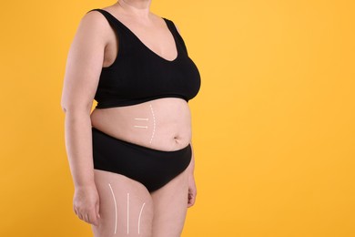 Woman with marks on body before cosmetic surgery operation on orange background, closeup. Space for text