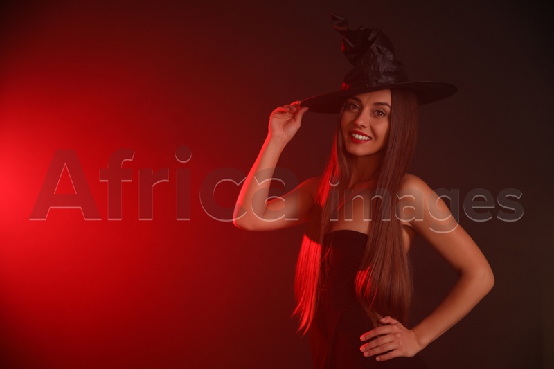 Young woman wearing witch costume on dark background, space for text. Halloween party