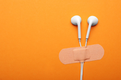 Wired earphones with sticking plaster on orange background, flat lay. Space for text