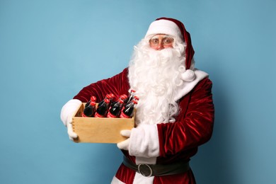 MYKOLAIV, UKRAINE - JANUARY 18, 2021: Santa Claus holding wooden crate full of Coca-Cola bottles on light blue background