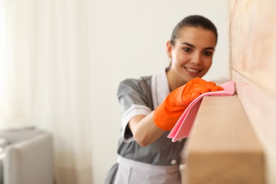 Young chambermaid wiping dust from furniture with rag in hotel room, closeup. Space for text