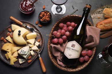 Flat lay composition with bottle of red wine and snacks on black table