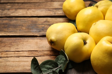 Fresh ripe organic quinces with leaves on wooden table, closeup. Space for text