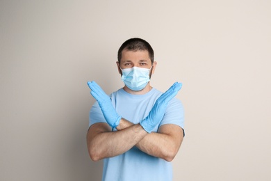Man in protective mask showing stop gesture on beige background. Prevent spreading of COVID‑19