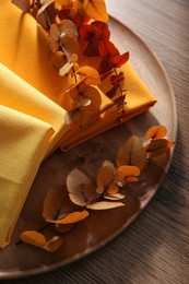 Tray with different kitchen napkins and decorative dry leaves on wooden table, top view