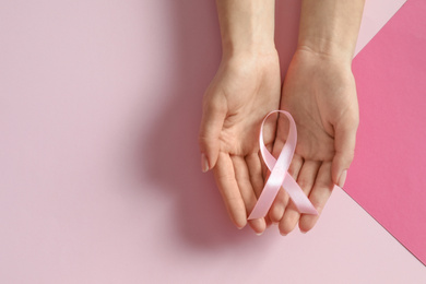 Woman holding pink ribbon on color background, top view with space for text. Breast cancer awareness