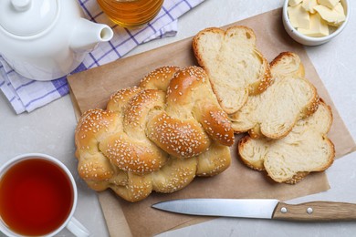 Cut homemade braided bread and freshly brewed tea on light grey table, flat lay. Traditional Shabbat challah