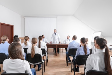 Photo of Senior doctor giving lecture near projection screen in conference room