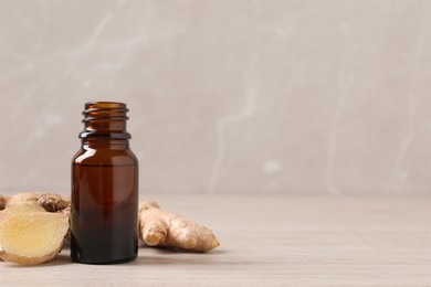Glass bottle of essential oil and ginger root on beige wooden table, space for text