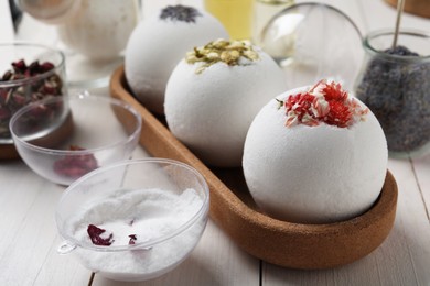 Different bath bombs and ingredients on white wooden table, closeup