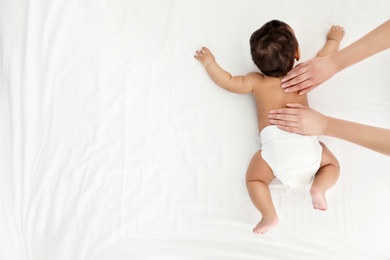 Top view of mother and her cute child on white bed, space for text. Baby massage and exercises