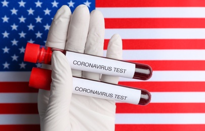 Scientist holding test tubes with blood samples over American flag, closeup. Coronavirus pandemic in USA