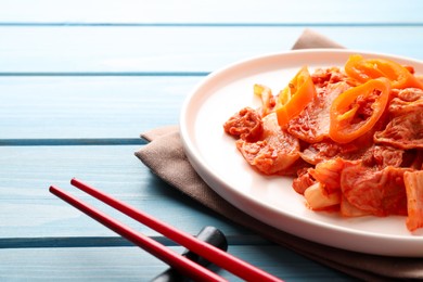 Photo of Plate of spicy cabbage kimchi with chili pepper and chopsticks on light blue wooden table, closeup