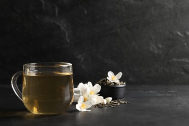 Glass cup of jasmine tea and fresh flowers on black table. Space for text