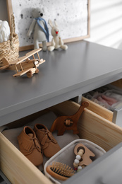 Open cabinet drawer with baby shoes and accessories in child room