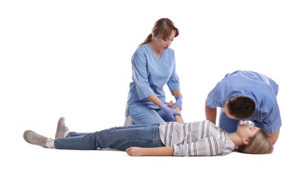 Medical workers in uniform performing first aid on unconscious woman against white background