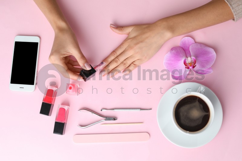 Woman applying nail polish on color background, above view