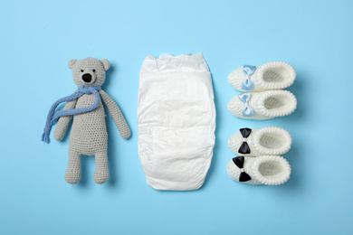 Diaper, toy bear and booties on light blue background, flat lay