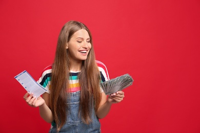 Portrait of happy young woman with lottery ticket and money on red background