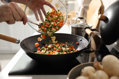 Man pouring mix of fresh vegetables into frying pan, closeup