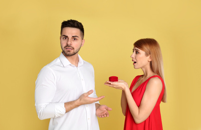 Young woman with engagement ring making proposal of marriage to her boyfriend on yellow background