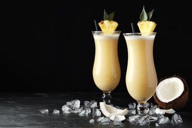 Tasty Pina Colada cocktails on dark table, space for text