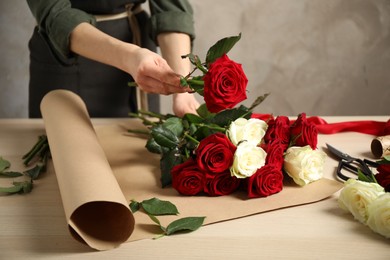 Photo of Woman making luxury bouquet of fresh roses at wooden table, closeup