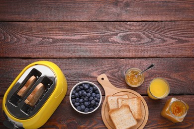 Yellow toaster with roasted bread, glass of juice, blueberries and jam on wooden table, flat lay. Space for text