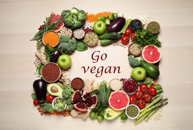 Phrase Go Vegan and fresh products on wooden background, flat lay