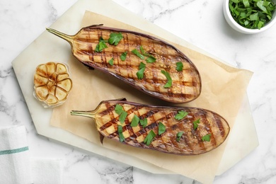 Delicious grilled eggplant halves with parsley on white marble table, flat lay