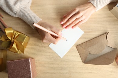 Woman writing message in greeting card on wooden table, top view