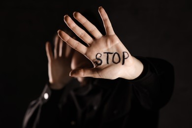 Photo of Woman with word Stop written on hand against dark background, closeup. Domestic violence concept