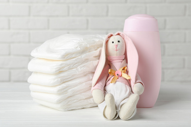 Baby diapers, toy bunny and bottle on wooden table against white brick wall