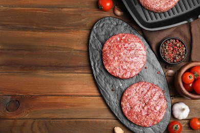 Raw hamburger patties with pepper and vegetables on wooden table, flat lay. Space for text