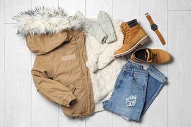 Flat lay composition with winter clothes and boots on white wooden background