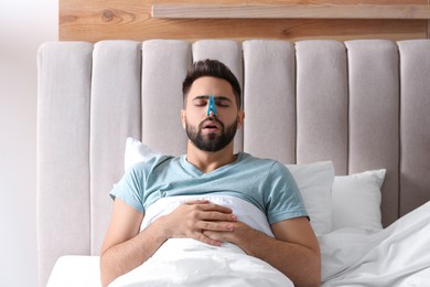Man with clothespin suffering from runny nose in bed