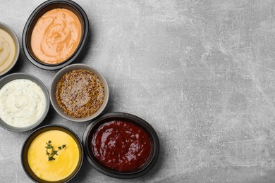 Many different sauces on grey table, flat lay. Space for text