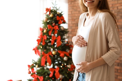 Pregnant woman near Christmas tree at home. Expecting baby