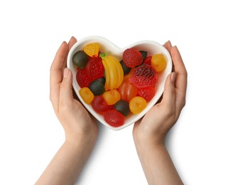 Woman holding heart shaped bowl with delicious gummy candies on white background, top view