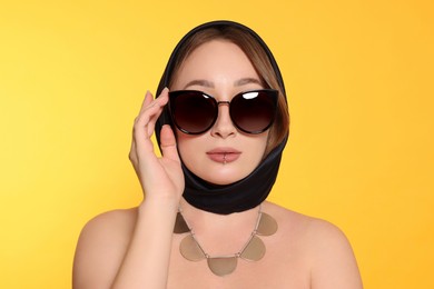 Young woman with lip piercing and sunglasses on yellow background