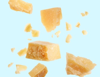 Pieces of delicious parmesan cheese flying on light background