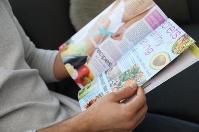 Man reading healthy food magazine on sofa at home, closeup