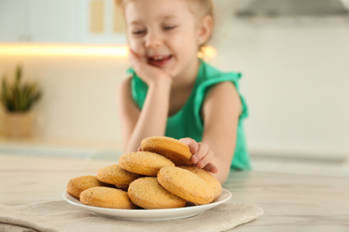Cute little girl at table with cookies in kitchen