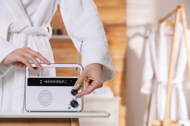 Woman in bathrobe turning volume knob on radio indoors, closeup. Space for text