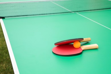 Rackets and ball on green ping pong table outdoors. Space for text
