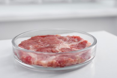 Petri dish with piece of raw cultured meat on white table indoors, closeup