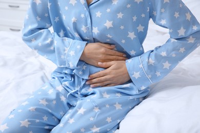 Young woman suffering from stomach ache on bed, closeup