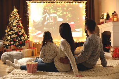 Family watching movie on projection screen in room decorated for Christmas. Home TV equipment