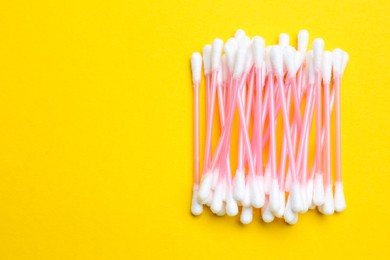Heap of cotton buds on yellow background, top view. Space for text